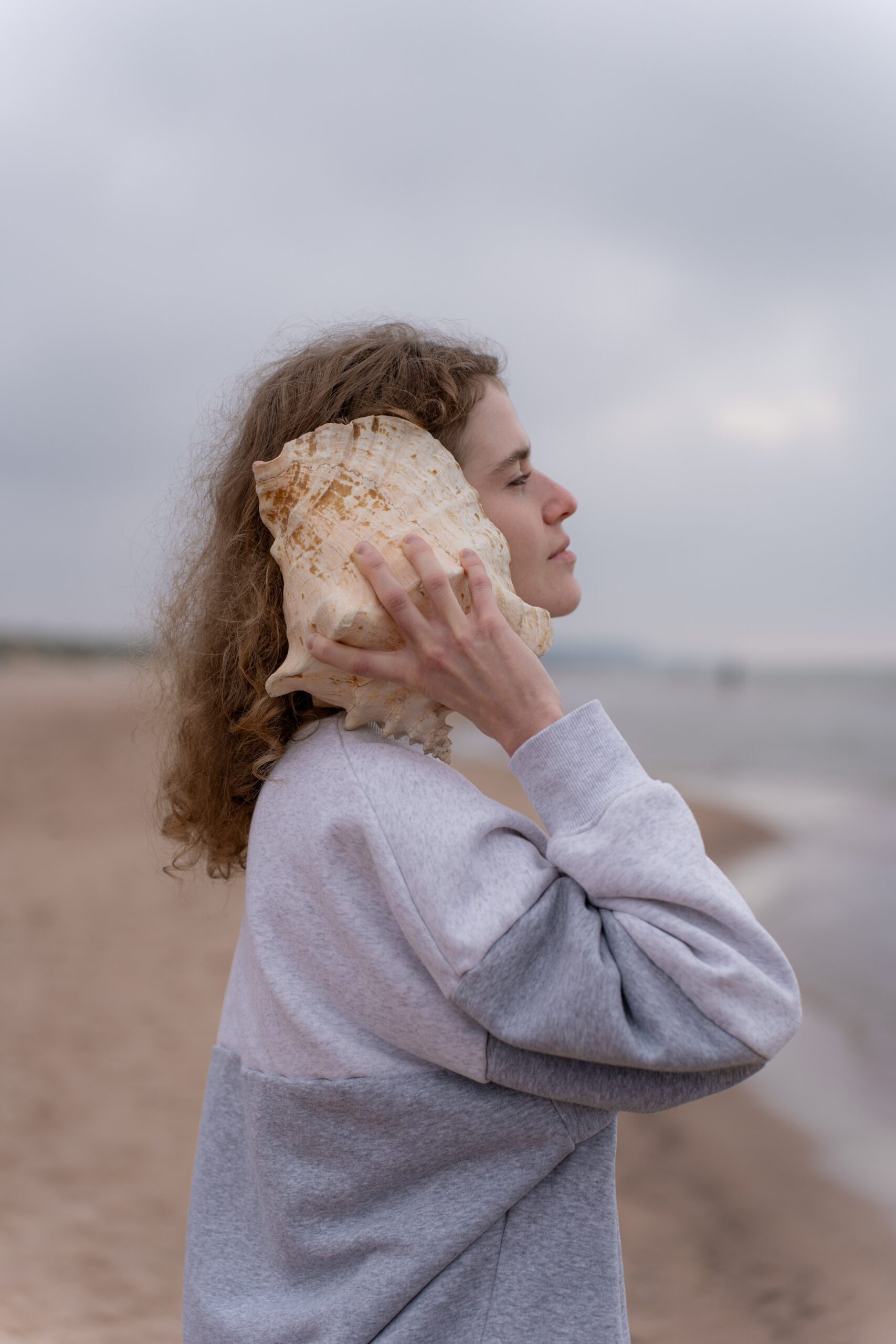 Femme tenant une conque contre son oreille sur une plage, stimulation du nerf vague